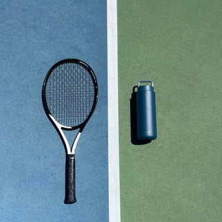 FELLOW Fellow Carter Carry Tumbler (32oz/946ml) in matte navy blue stainless steel with handle on tennis court