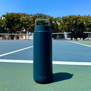Fellow Carter Carry Tumbler (32oz/946ml) in navy with stainless steel handle on basketball court