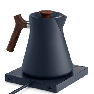 Fellow Corvo EKG Electric Kettle (120V) with matte black steel body and wooden handle on heating base
