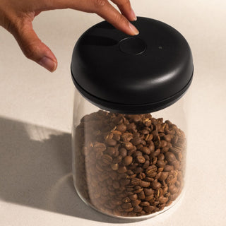 Fellow Electric Atmos Vacuum Canister - Clear Glass jar with black lid holding coffee beans and hand pressing top