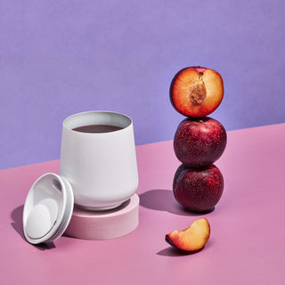 FELLOW Ruby Wine Tumbler (12oz/355ml) in white with magnetic lid beside stacked plums and fruit slice