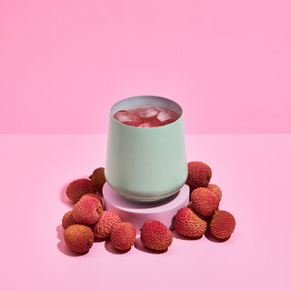 FELLOW Ruby Wine Tumbler (12oz/355ml) with ice, surrounded by fresh lychee fruit on pink background