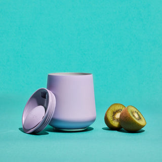 FELLOW Ruby Wine Tumbler (12oz/355ml) with ceramic coating and lavender stainless steel finish next to kiwi halves