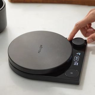 Fellow Tally Pro Precision Scale (Studio Edition) in matte black with user adjusting control knob on countertop