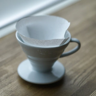 HARIO V60-01 (100 Pack) white paper filter placed inside a ceramic coffee dripper on wooden surface