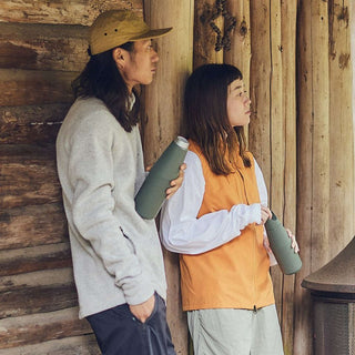 KINTO TRAIL Tumbler 1080ml stainless steel in muted green held by two people outdoors near wooden cabin