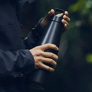 Person holding black KINTO TRAIL Tumbler 1080ml with matte finish and sturdy handle outdoors