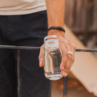 KINTO WATER Bottle 300ml held outdoors showing clear copolyester body and open lid design