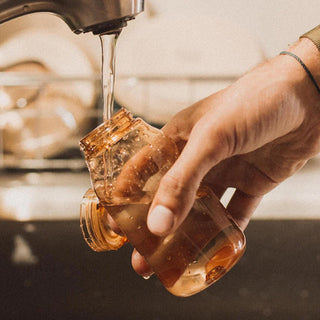 KINTO WATER Bottle 300ml in amber copolyester being rinsed under a kitchen faucet by hand