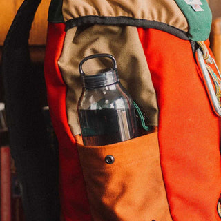 KINTO WATER Bottle 500ml with black cap in side pocket of orange and beige backpack outdoors