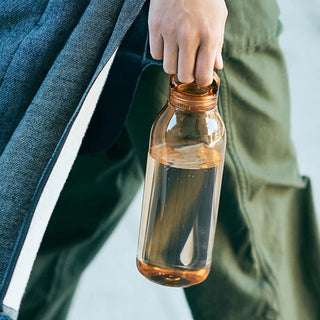 KINTO WATER Bottle 950ml held by hand, translucent amber copolyester with screw lid filled with water