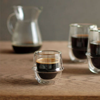 KINTO KRONOS Double Wall Espresso Cup 80ml filled with espresso on wooden surface with glass carafe background
