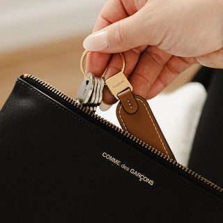 Orbitkey Loop Keychain with brown leather loop and stainless steel ring held near black zippered pouch