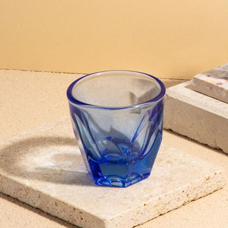 notNeutral VERO Cappuccino Glass 6oz in translucent blue glass with faceted texture on stone surface