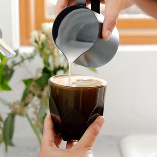 notNeutral VERO Cappuccino Glass 6oz held while frothy milk is poured from a stainless steel pitcher