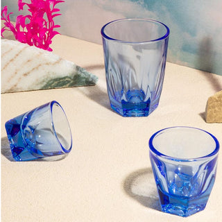 notNeutral VERO Latte Glass 12oz in translucent blue with faceted glass design on sandy surface