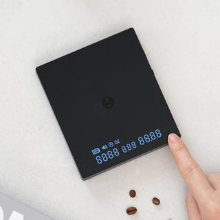 Timemore Black Mirror Mini Coffee Scale showing blue digital display with finger pressing button on black surface