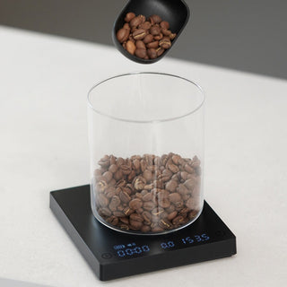 Timemore Black Mirror Mini Coffee Scale measuring fresh coffee beans in a clear glass container