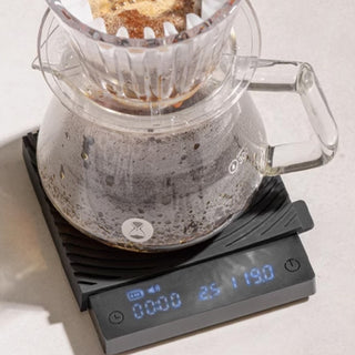 Timemore Black Mirror Mini Coffee Scale showing digital weight with glass coffee carafe brewing drip coffee