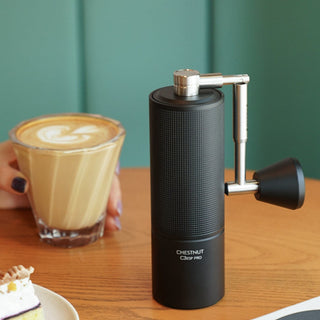 Timemore Chestnut C3 ESP PRO Grinder in black aluminum with textured grip beside a latte glass on wooden table