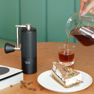 Timemore Chestnut C3 ESP PRO Grinder in black aluminum with textured grip on wooden table next to coffee and dessert