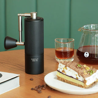 Timemore Chestnut C3 ESP PRO Grinder with textured black aluminum body on wooden table near dessert and coffee