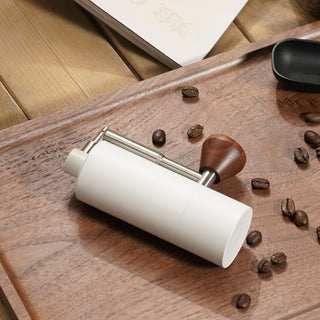 Timemore Chestnut Nano 3 Grinder white aluminum body with walnut handle on wooden tray and coffee beans scattered