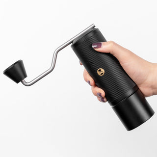Timemore Chestnut X Lite hand grinder held, showing black ribbed stainless steel body and crank handle