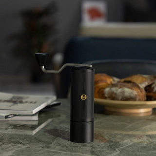 Timemore Chestnut X Lite black hand grinder with stainless steel handle on marble table by pastries