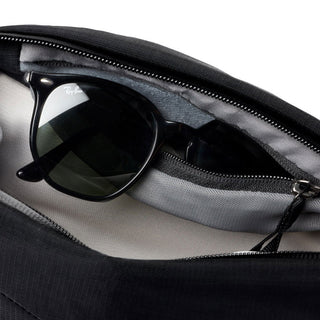 Bellroy Venture Sling 6L black recycled fabric pouch holding black sunglasses with zipper open