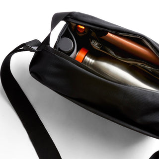 Bellroy Venture Sling 6L in black showing organized interior with metal water bottle and tech accessories
